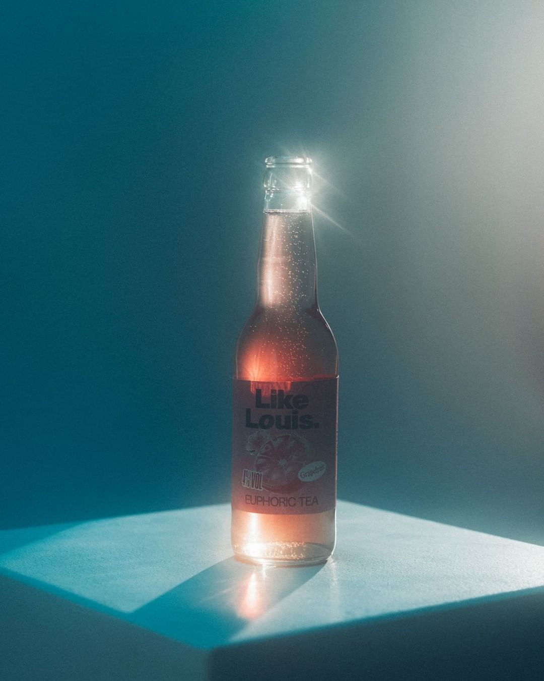 A bottle of Like Louis Euphoric Tea is showcased against a blue gradient backdrop, sitting atop a blue surface with dramatic lighting.