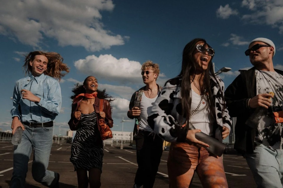 Group of five young adults smiling and walking on a rooftop parking lot under a partly cloudy sky, bathed in sunlight.