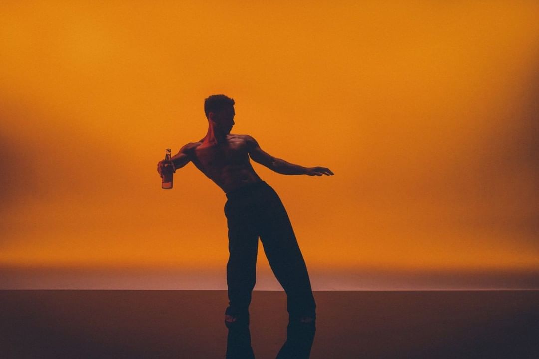 Athletic man in silhouette, posing with a beer bottle against an orange backdrop, creating a striking and stylized studio shot.