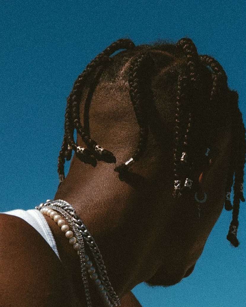 Stylish man with braids and pearl necklace against a serene blue sky. Fashionable jewelry and hairstyle in an outdoor setting.