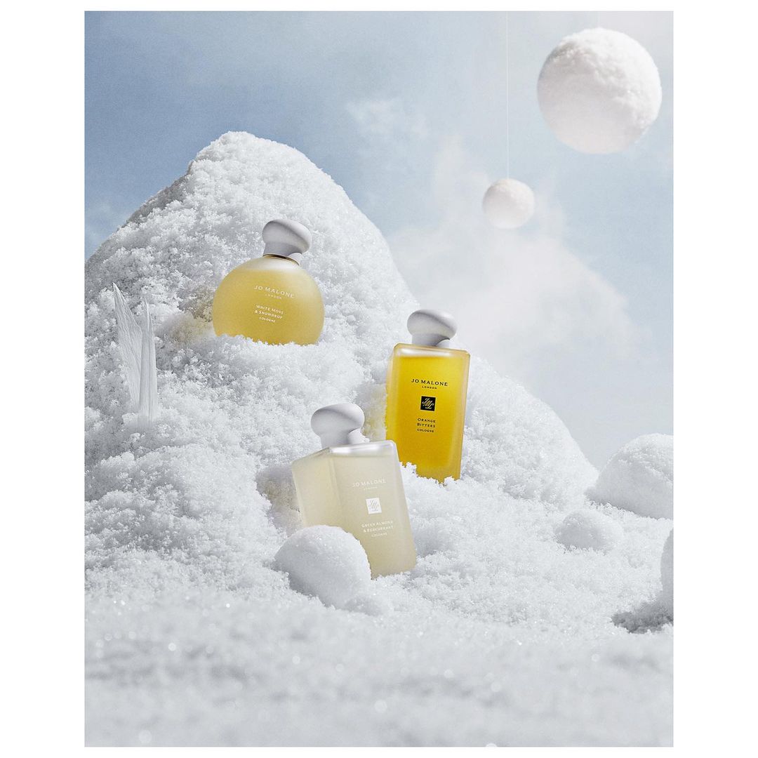 Three bottles of Jo Malone London fragrance are arranged on a snow-covered surface, with soft, diffused lighting and snowy orb props.