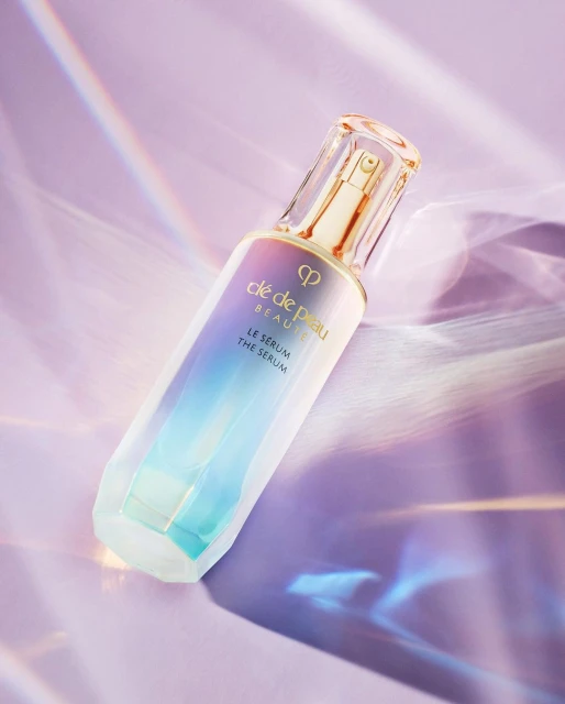 Serum bottle of Clé de Peau Beauté in a studio shot against a purple backdrop, highlighting its multifaceted surface.