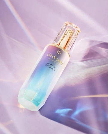 Serum bottle of Clé de Peau Beauté in a studio shot against a purple backdrop, highlighting its multifaceted surface.