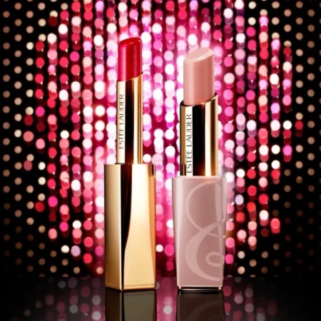 Two Estee Lauder lipsticks, one red and one nude, stand against a pink bokeh background, showcasing beauty and cosmetic elegance.