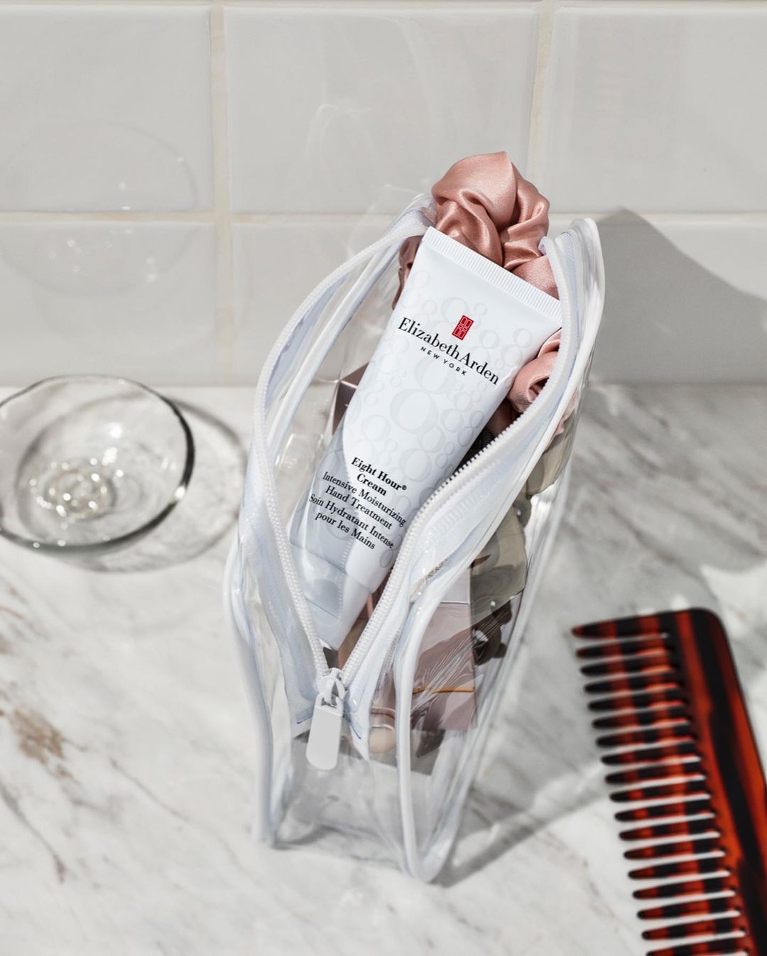 Cosmetic bag featuring Elizabeth Arden Eight Hour Cream, scrunchies, and a comb on a tiled surface, showcasing beauty and personal care.