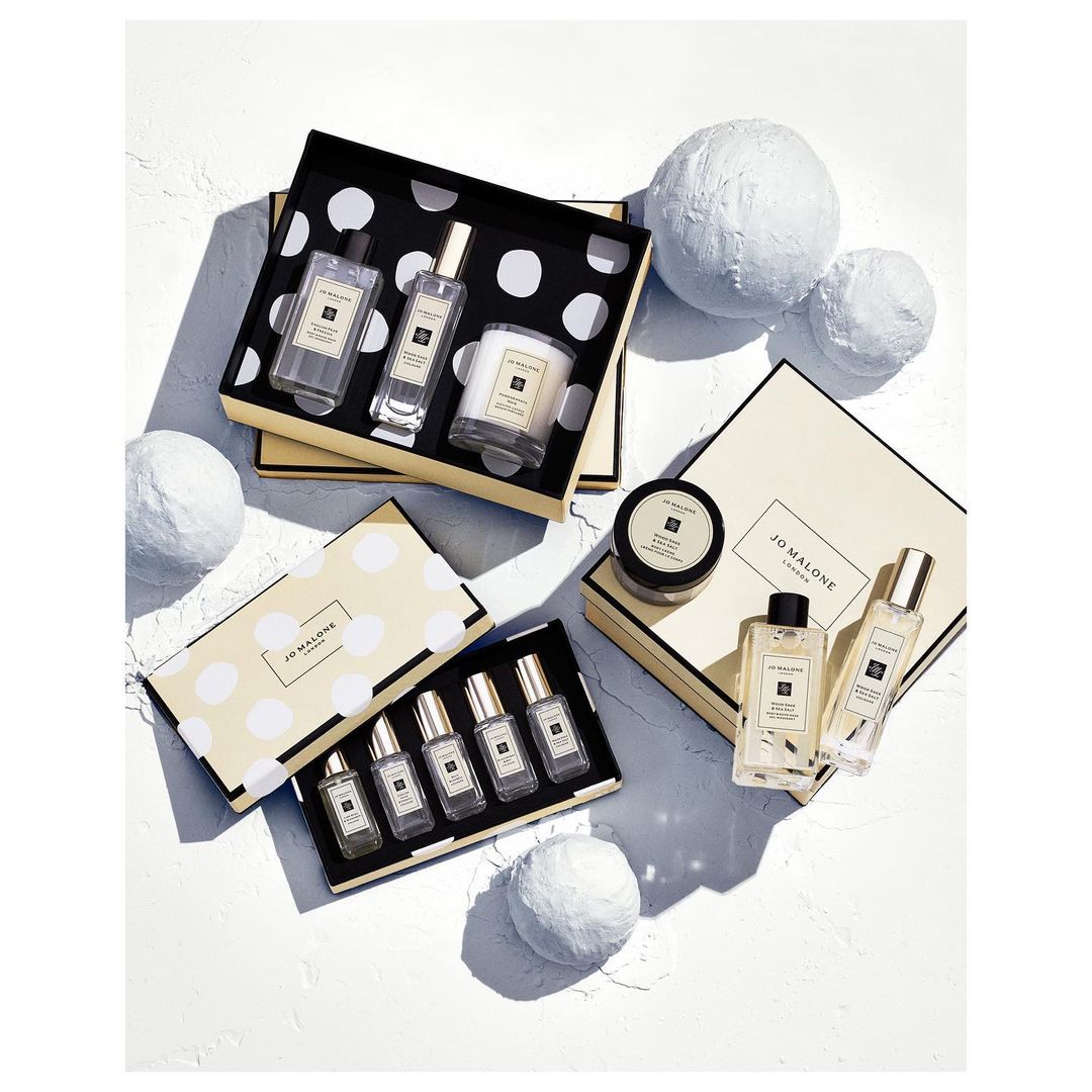 Overhead studio shot of multiple Jo Malone product sets in their respective boxes, with decorative white styrofoam balls on a white surface.