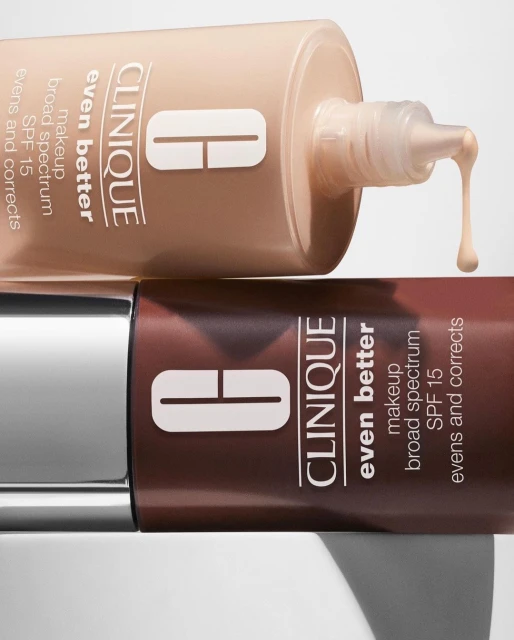Close-up of two Clinique Even Better makeup bottles in different shades, stacked, with a drop of makeup falling from the top bottle.