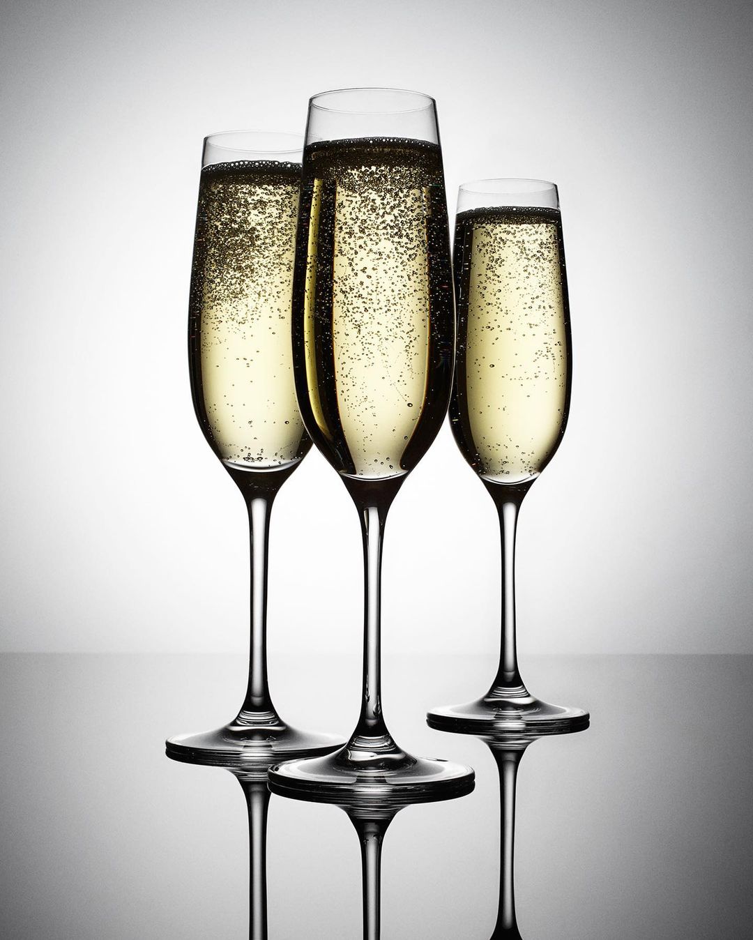 Three champagne flutes filled with sparkling wine and bubbles against a bright gradient background, creating an elegant still life.