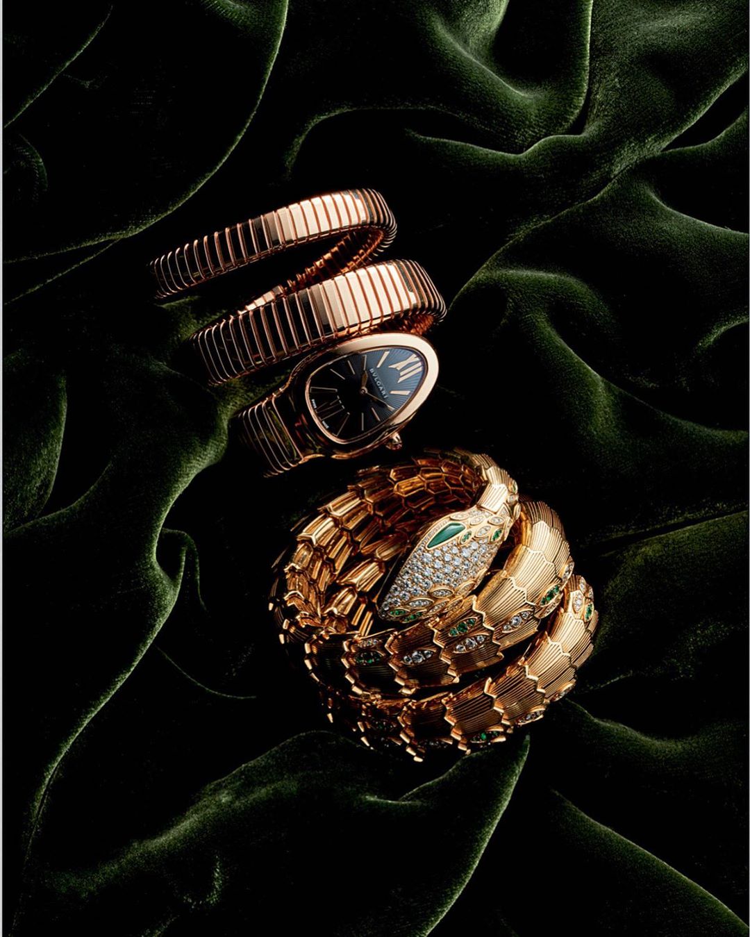 Two gold Bulgari Serpenti watches coiled on a green velvet surface. One watch is snake-shaped with gemstone accents.