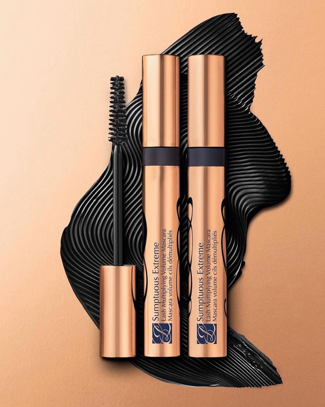 Close-up of two Sumptuous Extreme mascaras by Estee Lauder with applicator on tan background, beauty and cosmetics product photography.