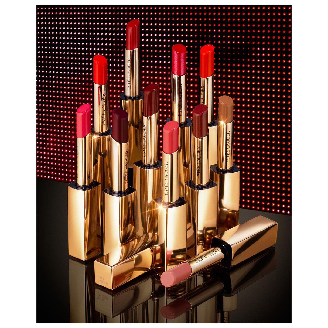Collection of lipstick tubes in various shades of red, pink, and brown, displayed against a red and black dotted background.