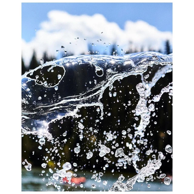 Clear water splash close-up with blurred trees and a cloudy sky in the background creates a refreshing nature scene, outdoors on a bright day.