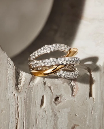 Close-up of a modern statement ring featuring interconnected bands of gold and diamond pavé, resting on a textured surface.