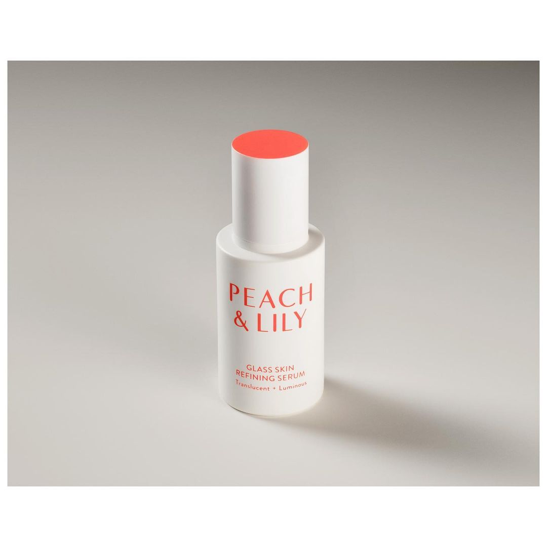 Peach & Lily glass skin refining serum in white bottle with coral cap on white surface in studio lighting for beauty product shot.