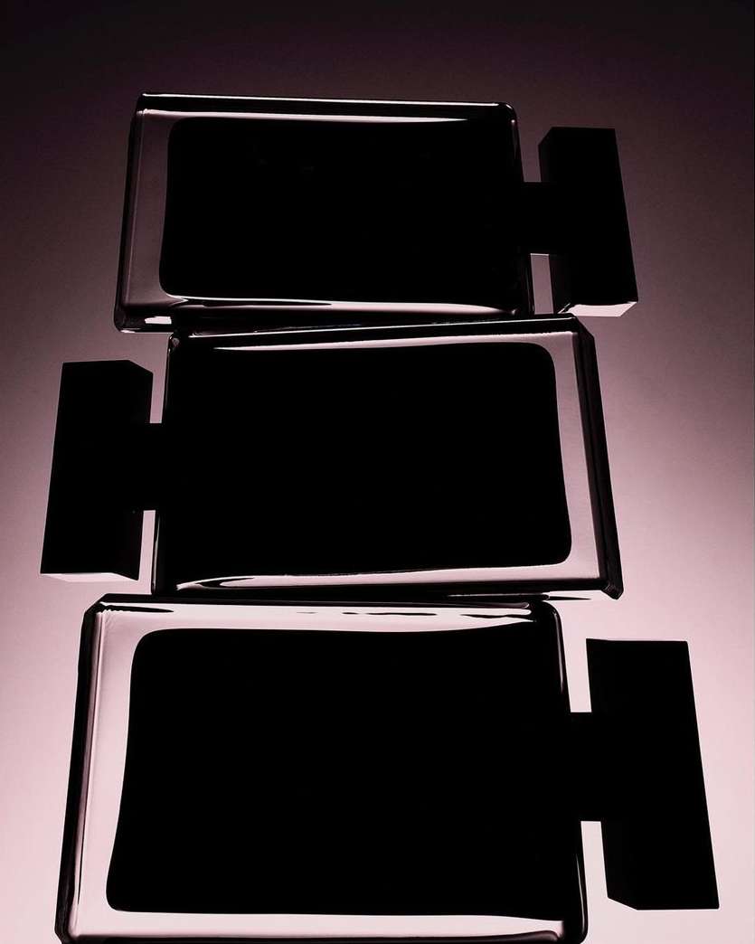 Three rectangular glass bottles are stacked vertically, casting reflections in a studio setting with a dark background.