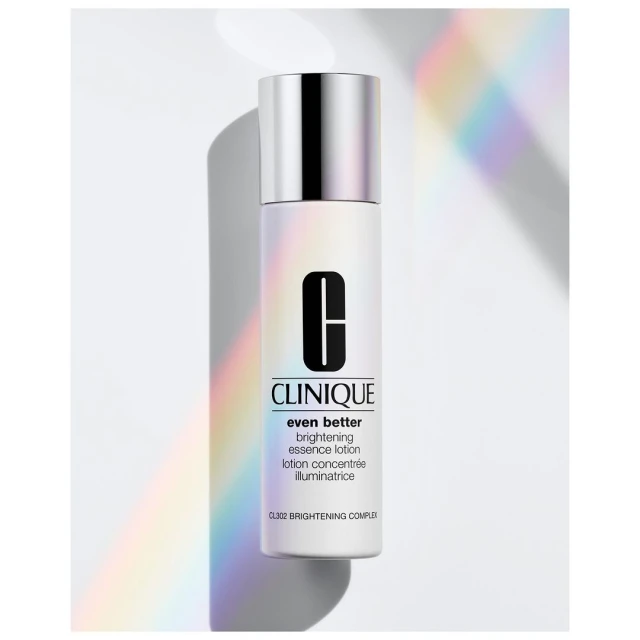 Close-up of a Clinique Even Better brightening essence lotion bottle with a silver cap on a white surface with pastel light.