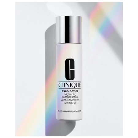 Close-up of a Clinique Even Better brightening essence lotion bottle with a silver cap on a white surface with pastel light.