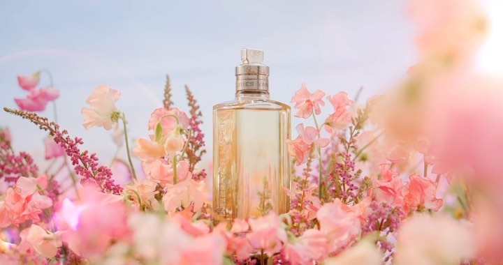 Close-up of a perfume bottle surrounded by pink and white flowers, set against a pale sky, creating a soft, floral fragrance visual.