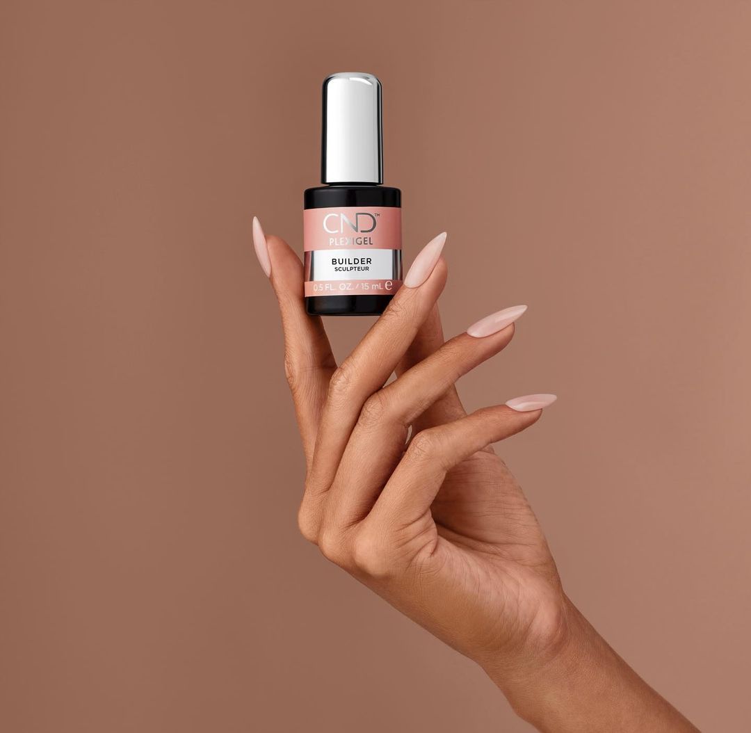 A woman's manicured hand displays a bottle of CND PLEXIGEL Builder sculpting gel, nails painted in a matching neutral color.