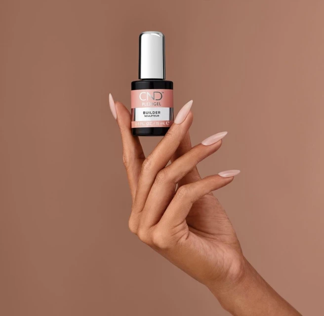 A woman's manicured hand displays a bottle of CND PLEXIGEL Builder sculpting gel, nails painted in a matching neutral color.