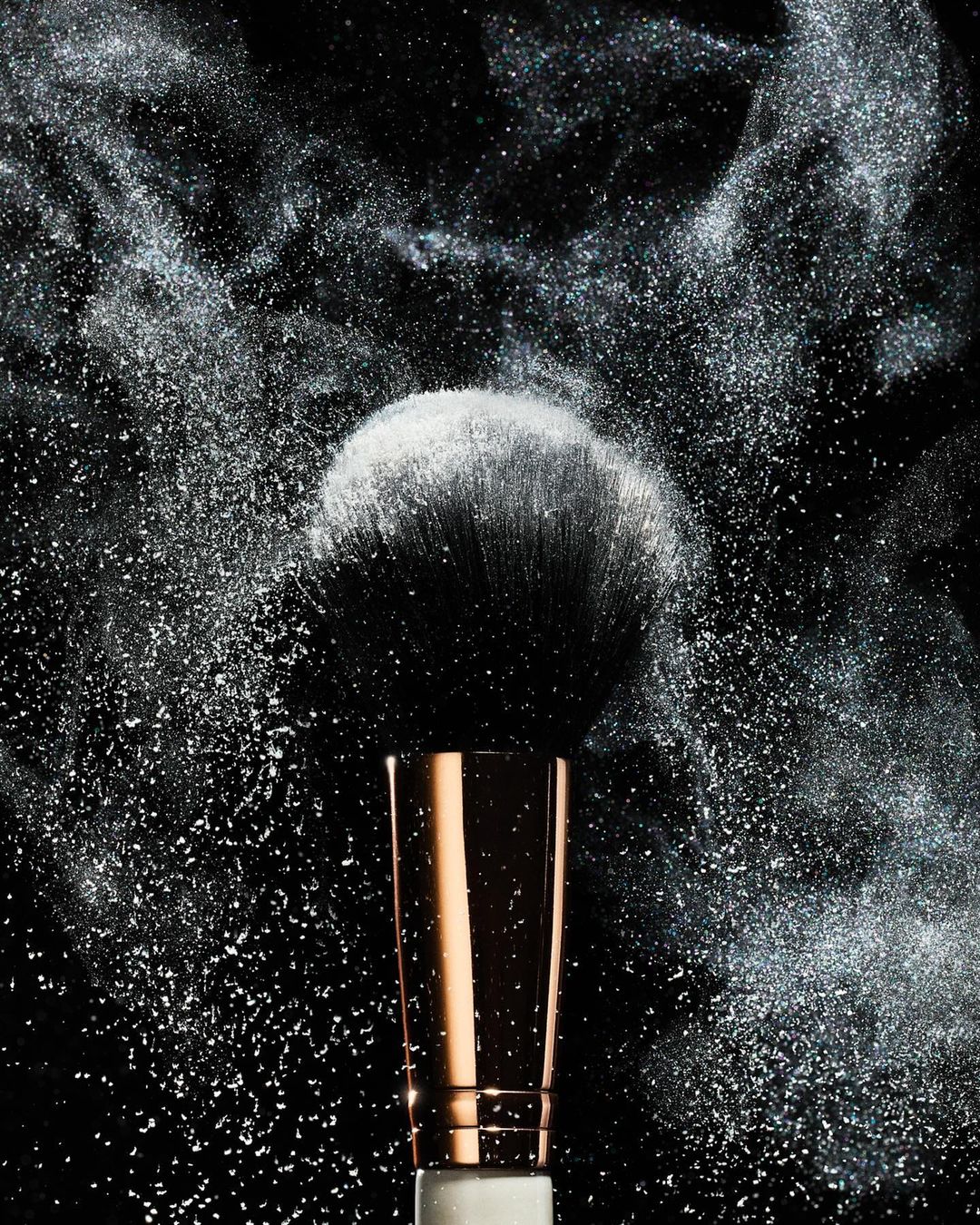 Makeup brush with white powder dust against a dark background, close-up studio shot for beauty or cosmetics promotion.
