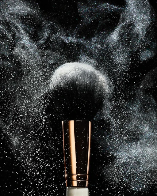 Makeup brush with white powder dust against a dark background, close-up studio shot for beauty or cosmetics promotion.