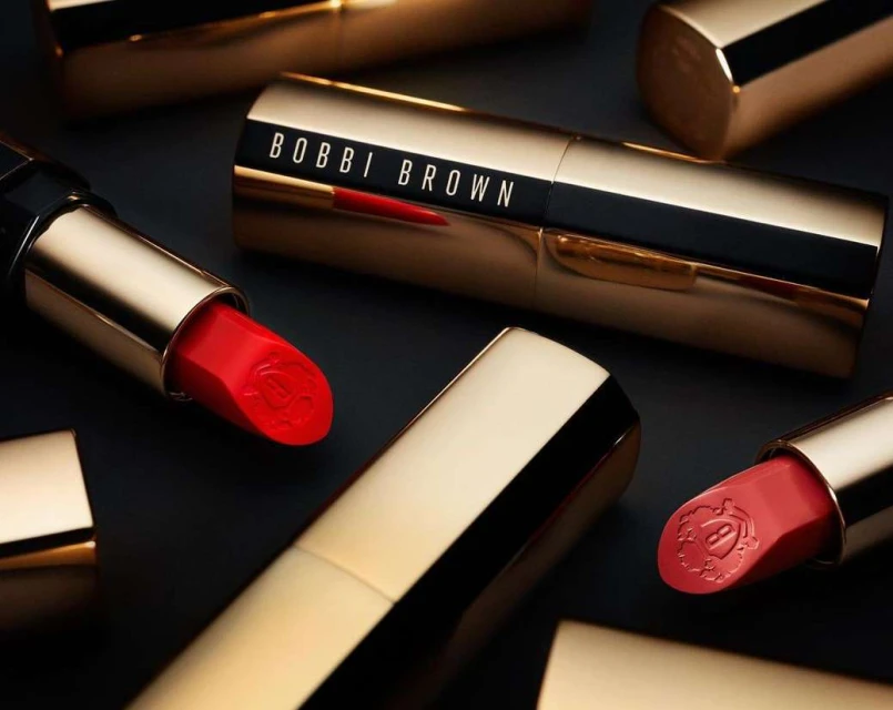 Bobbi Brown red lipstick tubes with gold casing on a dark background. Beauty and fashion product shot for cosmetics brand.