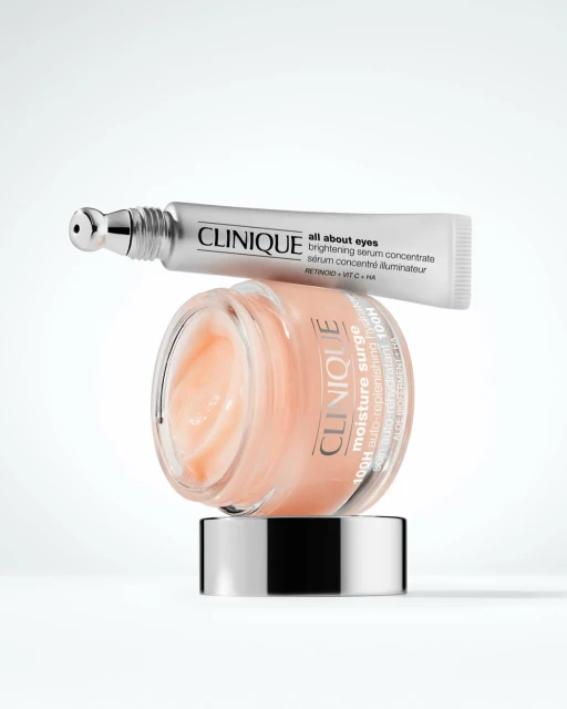 Two Clinique skincare products, including 'All About Eyes' serum and 'Moisture Surge' cream, arranged on a white background for beauty.