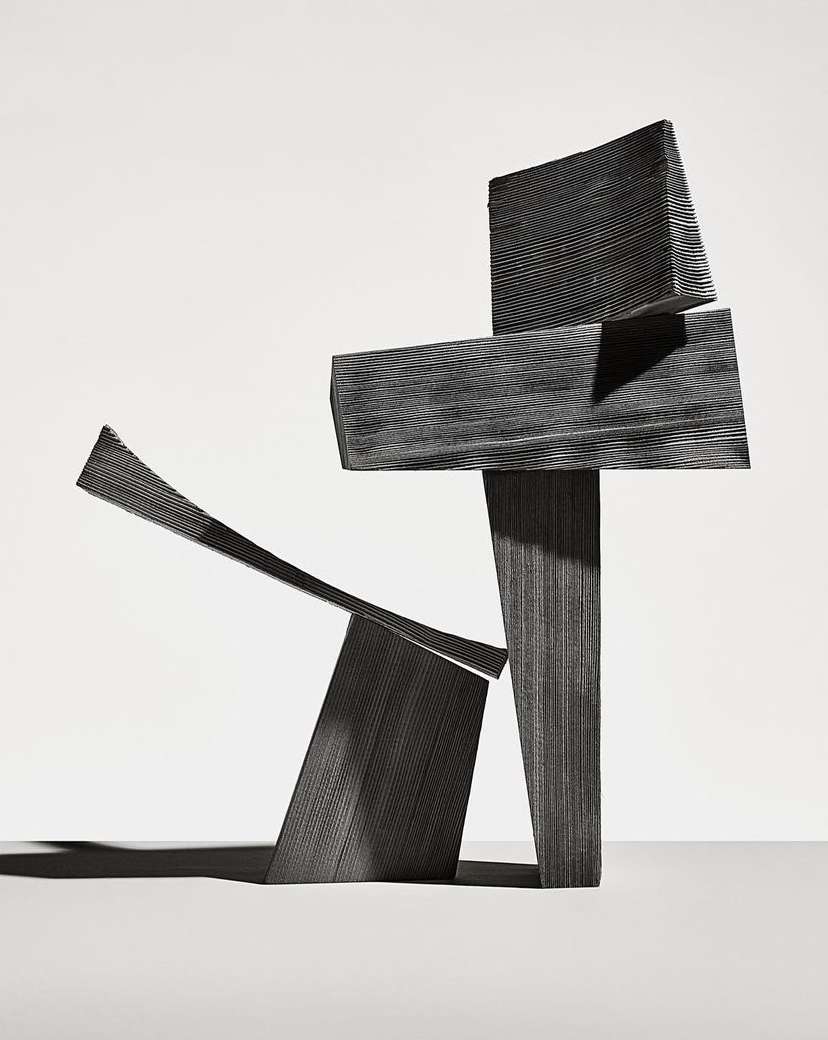 Abstract sculpture composed of geometric shapes in grayscale, featuring varied textures and dynamic angles, against a light backdrop.