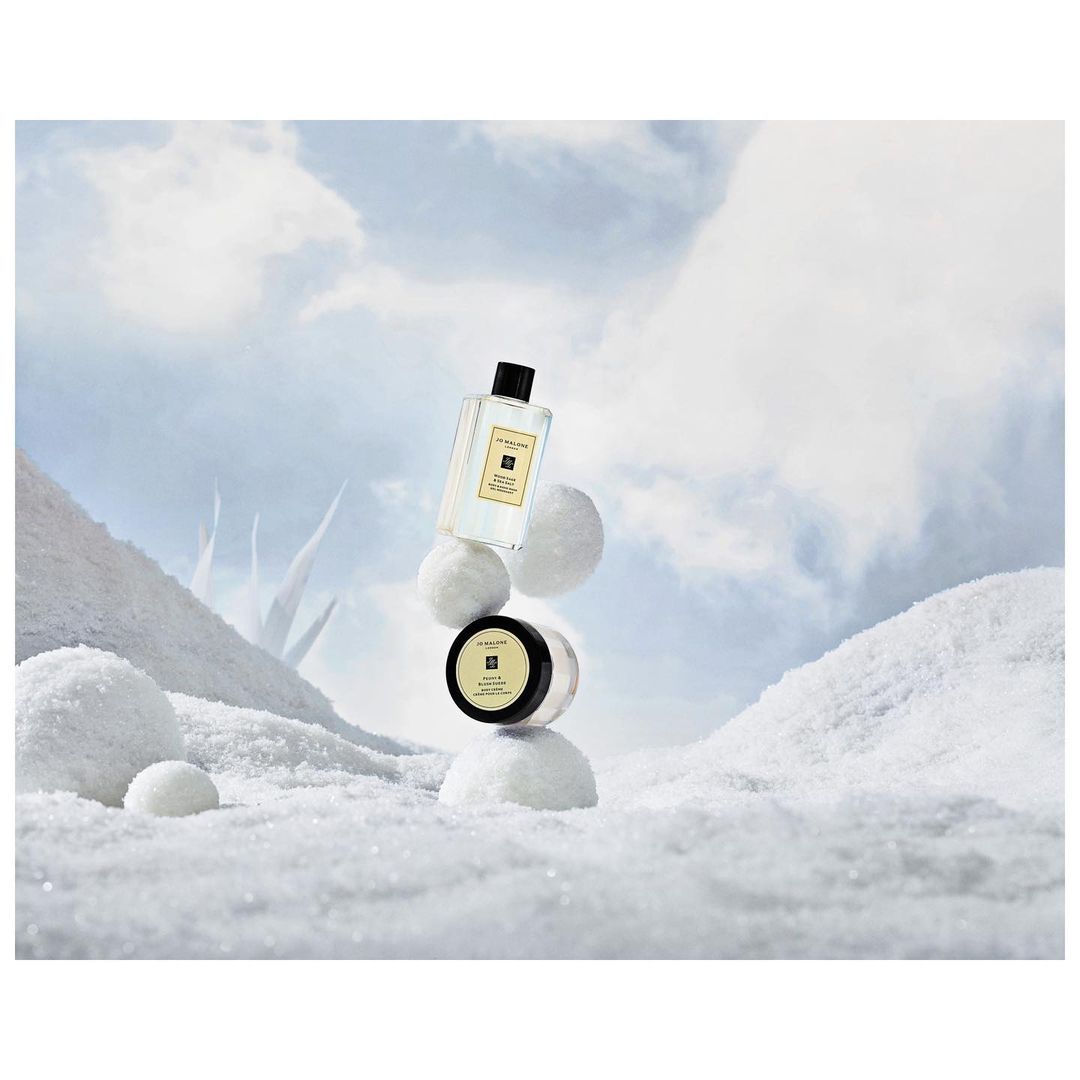 Jo Malone London perfume and body cream product shot on snowy surface with cloudy sky background, ideal for beauty and fragrance ads.