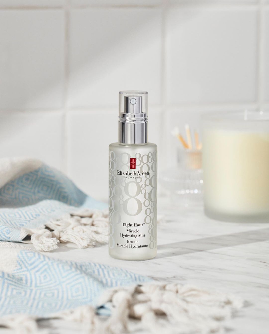 Silver Elizabeth Arden Eight Hour Miracle Hydrating Mist spray bottle on a white marble surface with a white and blue towel.