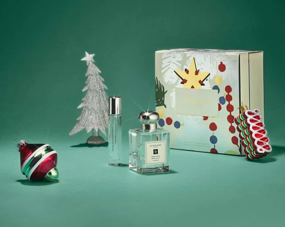 Festive still life showcasing perfume bottles, holiday ornaments, and a gift box against a green backdrop. Elegant holiday presentation.