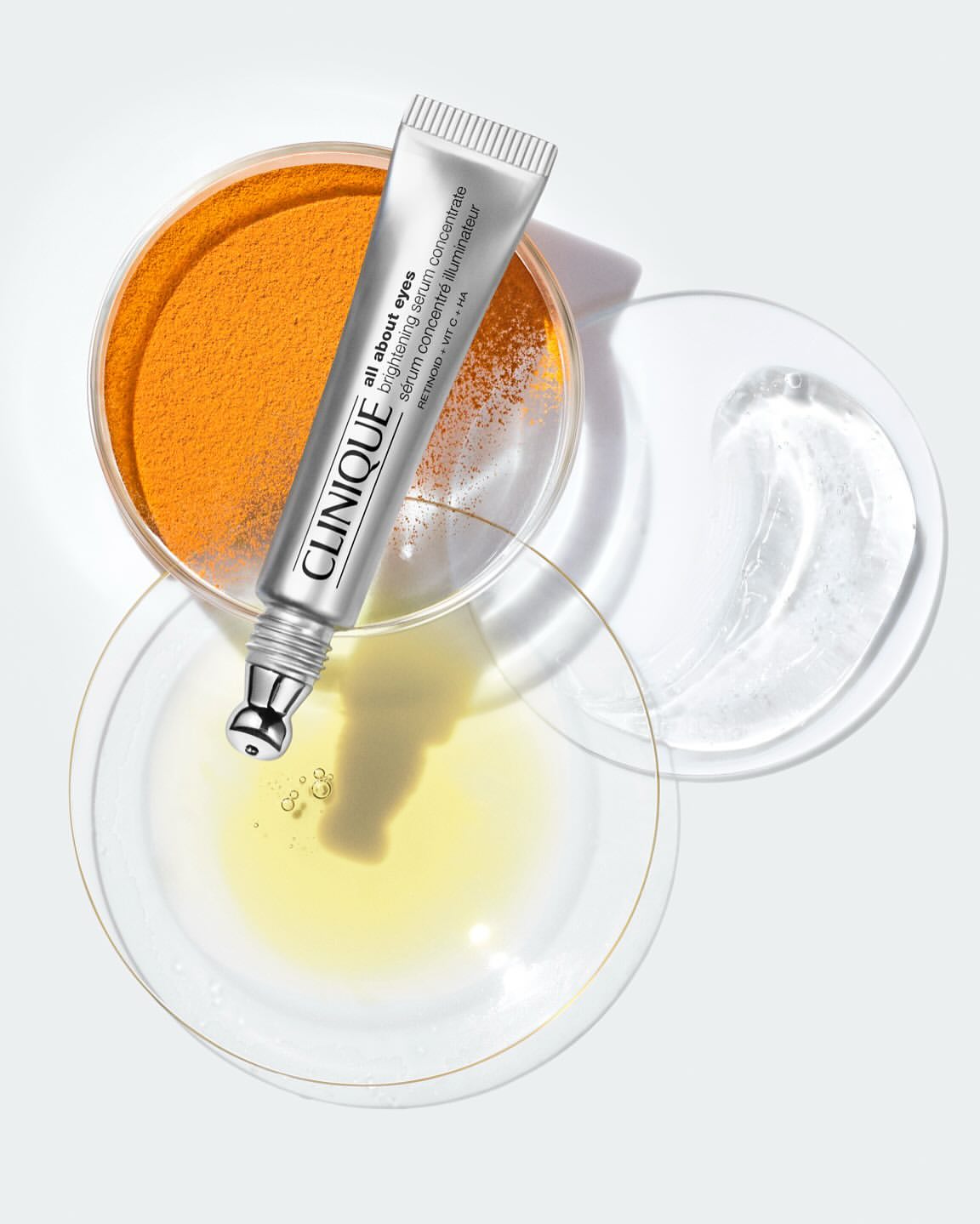 Clinique 'All About Eyes' brightening serum concentrate sits atop petri dishes with skincare ingredients against a light background.