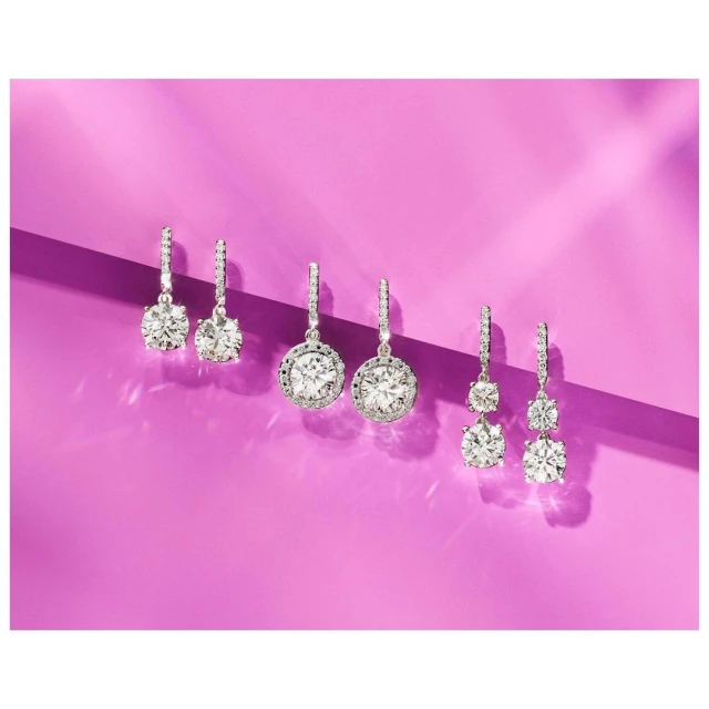 Three pairs of diamond drop earrings with varying stone shapes and halo settings on a bright purple background, jewellery photography.