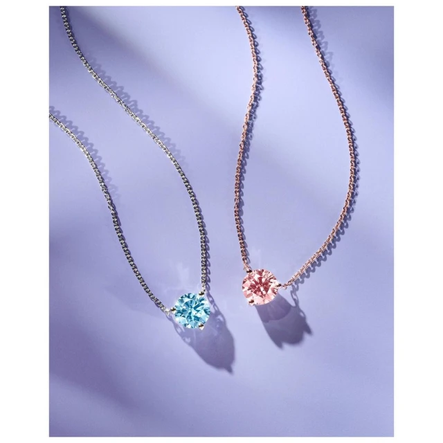 Close-up studio shot of a pair of delicate necklaces, one silver with an aquamarine stone, the other rose gold with a light pink stone.