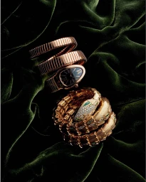 Rose gold jewellery pieces including a coiled watch and a serpent-shaped bracelet rest on dark green velvet fabric.