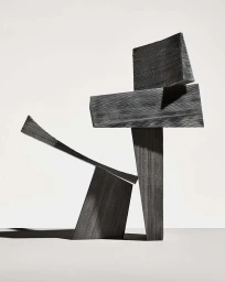 Abstract black wooden sculpture with textured geometric planks balancing on a light background