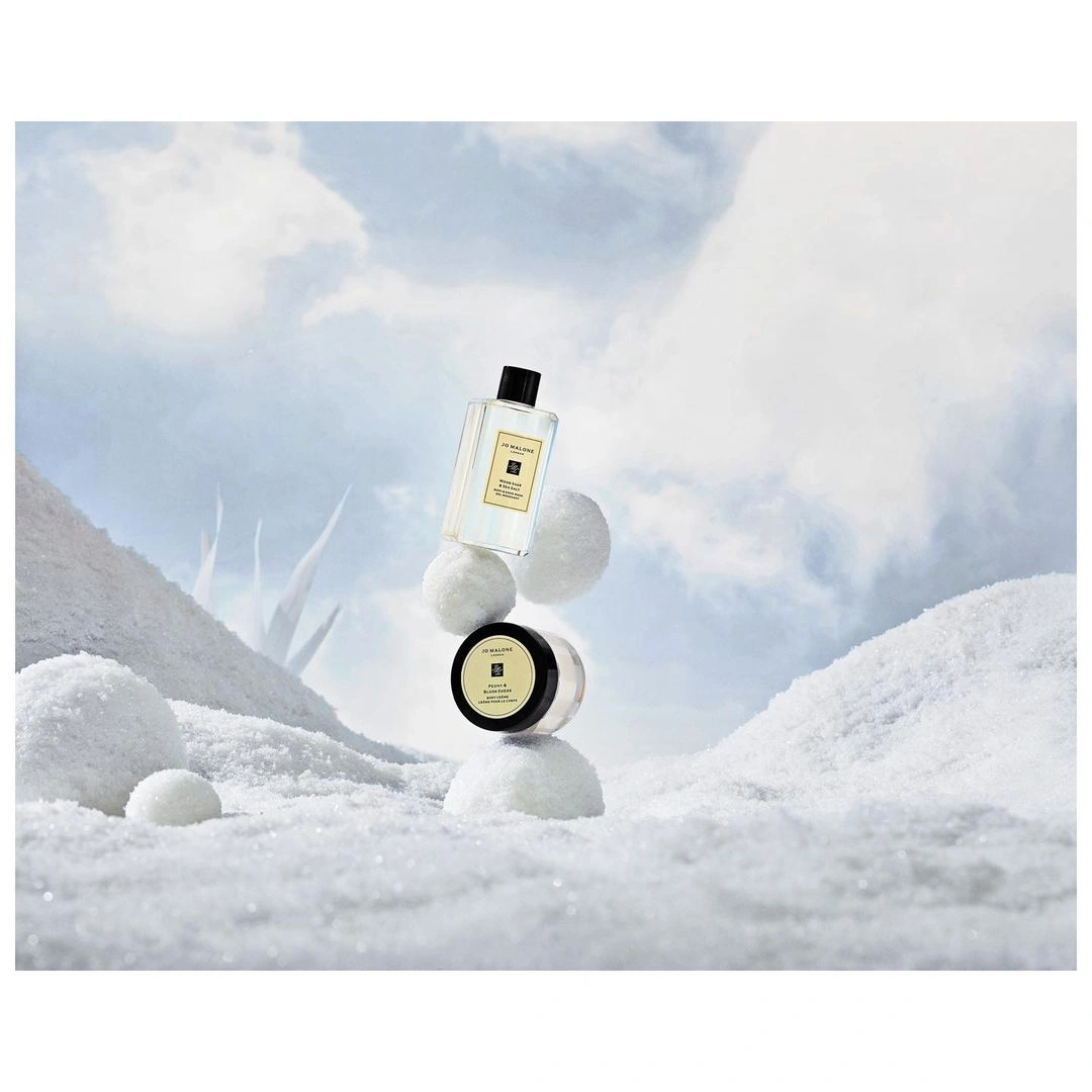 Jo Malone fragrance bottle and jar balanced on snowballs against a winter sky