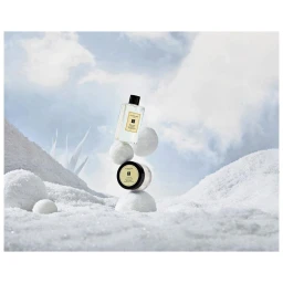Jo Malone fragrance bottle and jar balanced on snowballs against a winter sky