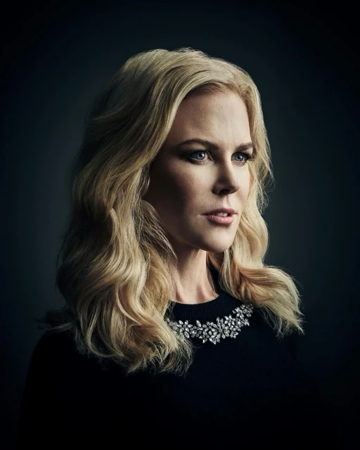 Close-up portrait of a blonde woman with shoulder-length wavy hair, wearing a dark top with a jeweled necklace against a dark background.