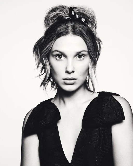 Black and white portrait of a young woman with her hair up, wearing a black dress with a V-neck, against a white background.