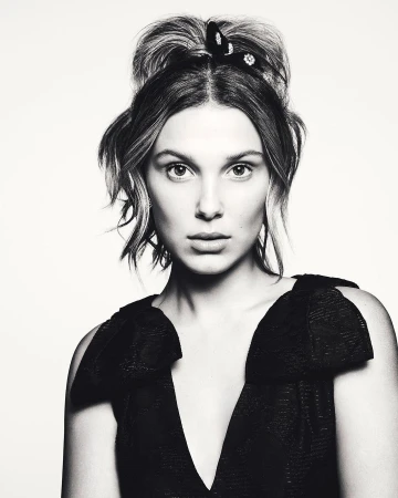 Black and white portrait of a young woman with her hair up, wearing a black dress with a V-neck, against a white background.
