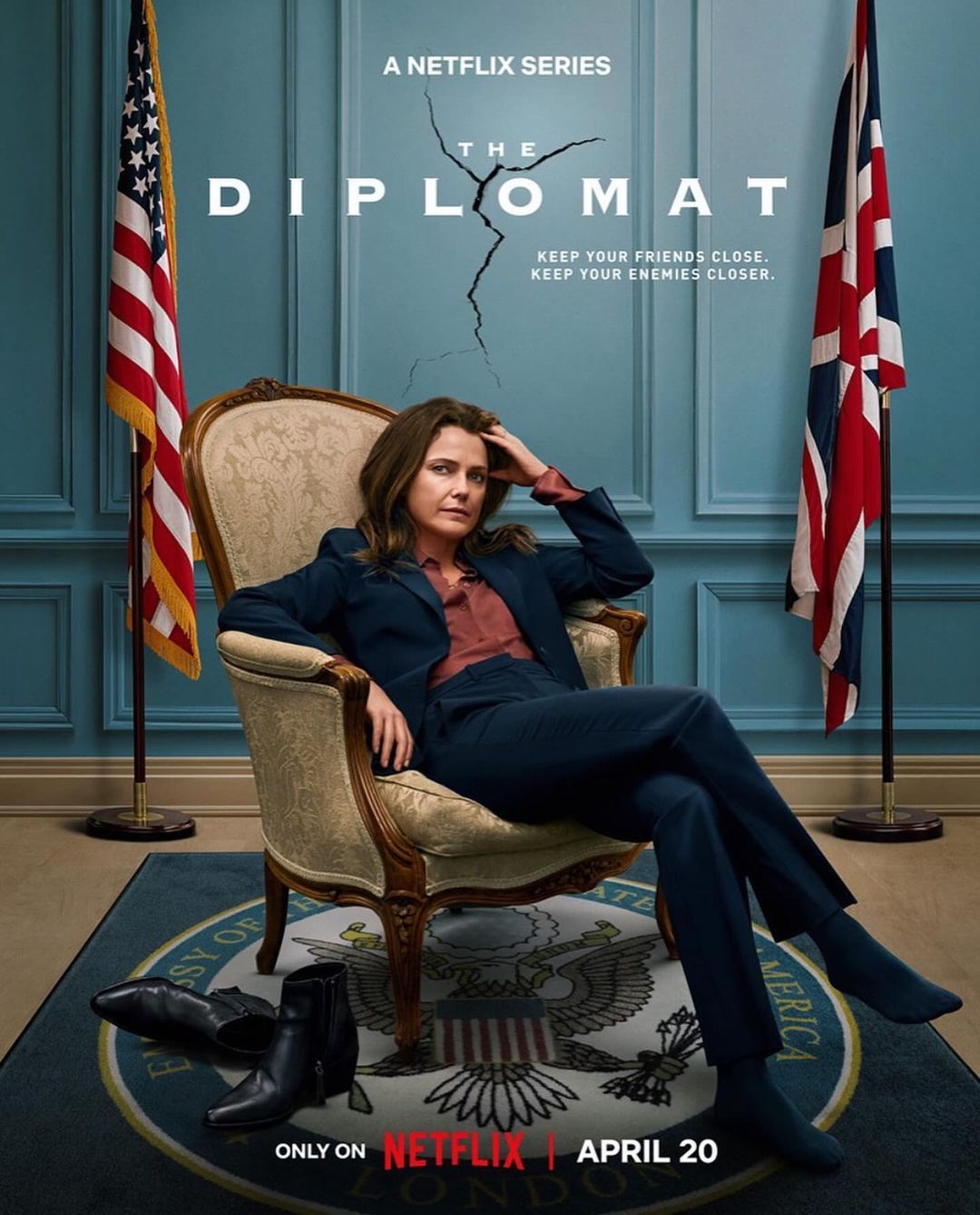 Poster for The Diplomat featuring a woman in a navy suit sitting in a chair with the United States and British flags in the background.