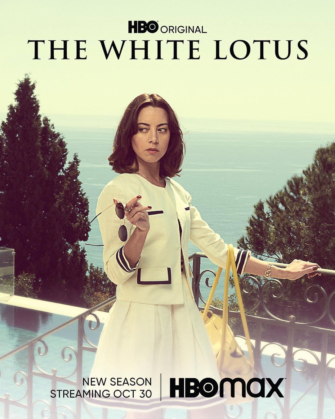 Aubrey Plaza in a promotional poster for The White Lotus Season 2, standing near a pool with the ocean as a backdrop.