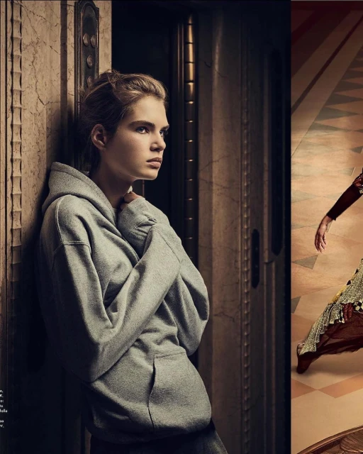 Portrait of a young adult female in a grey hoodie leaning against a marble doorway, looking left with a neutral expression in soft light.