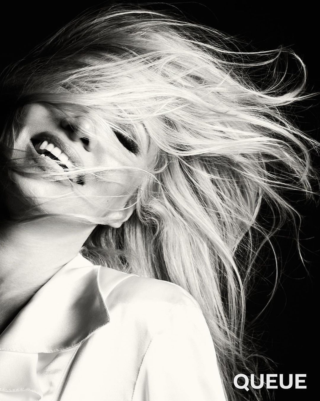 Black and white portrait of an adult female with flowing blonde hair, a white collared shirt, and a joyful facial expression.