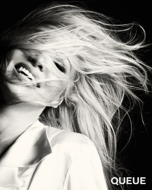 Black and white portrait of an adult female with flowing blonde hair, a white collared shirt, and a joyful facial expression.