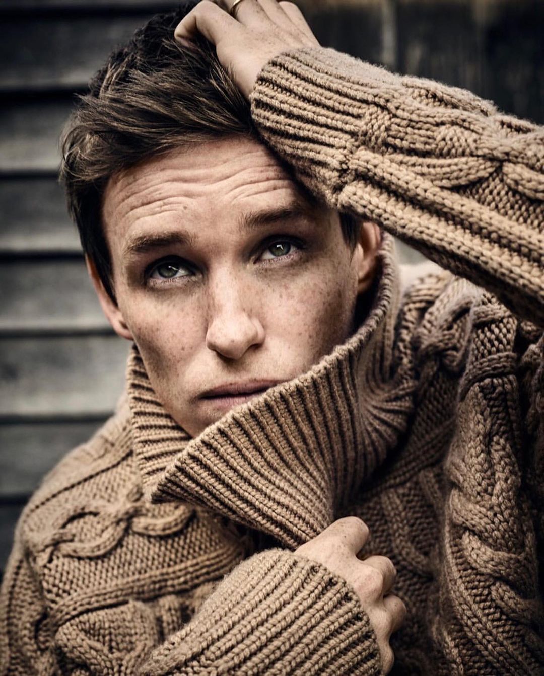Portrait of adult male with fair skin, brown hair, freckles, light eyes, wearing a chunky knit tan turtleneck sweater, looking up.