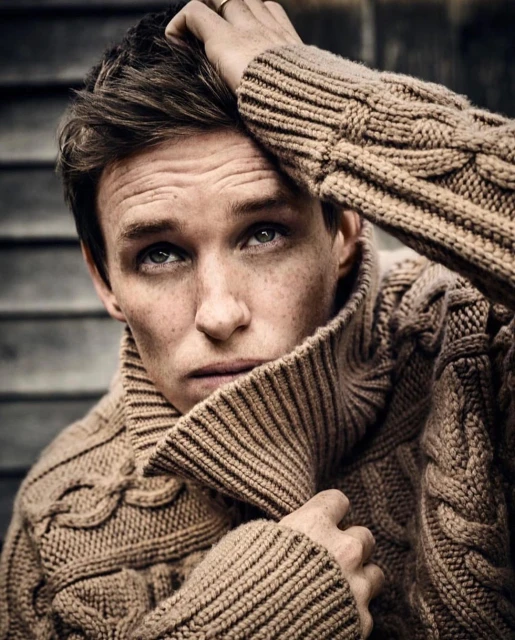 Portrait of adult male with fair skin, brown hair, freckles, light eyes, wearing a chunky knit tan turtleneck sweater, looking up.