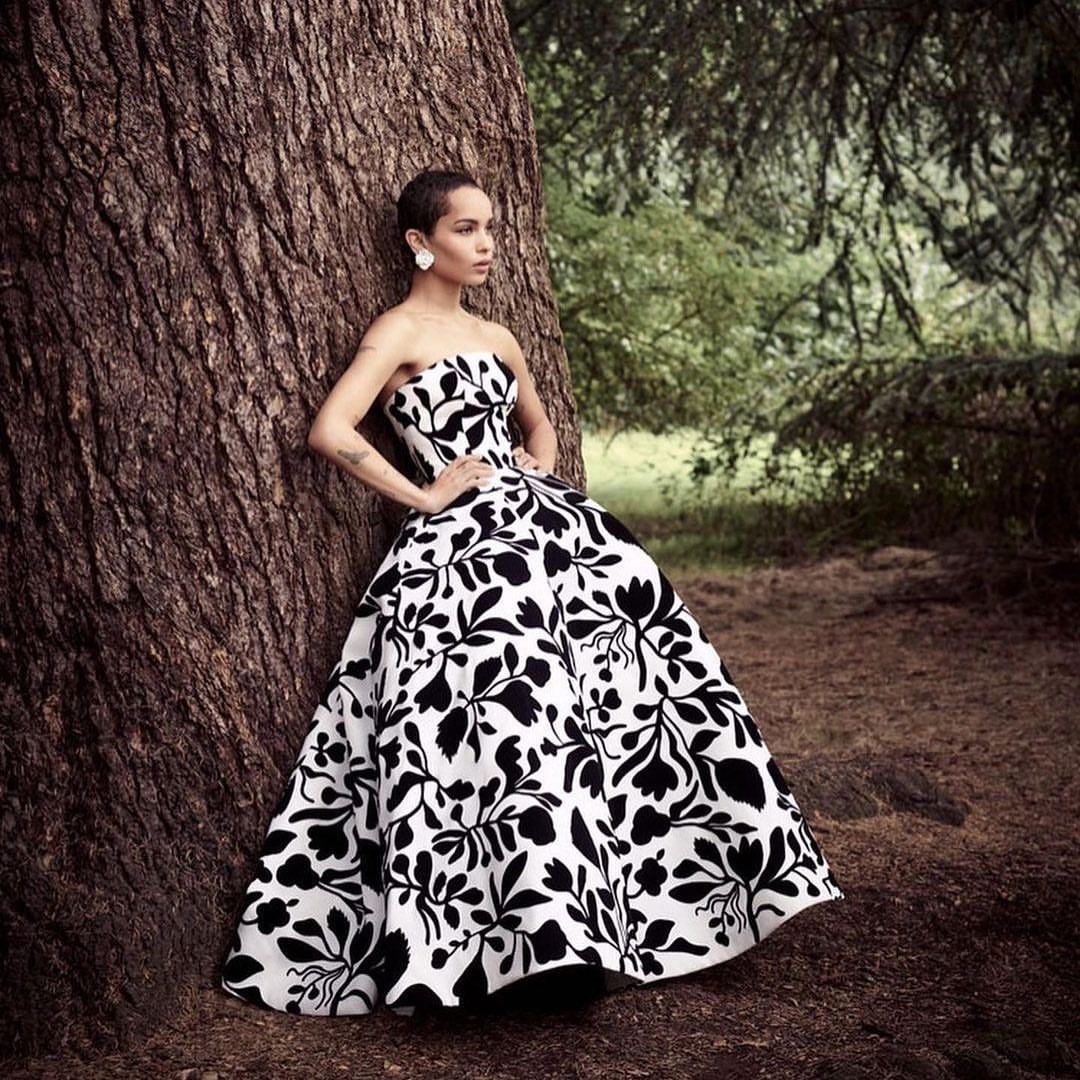 Elegant woman in a strapless black and white floral gown stands by a large tree in a natural outdoor setting.